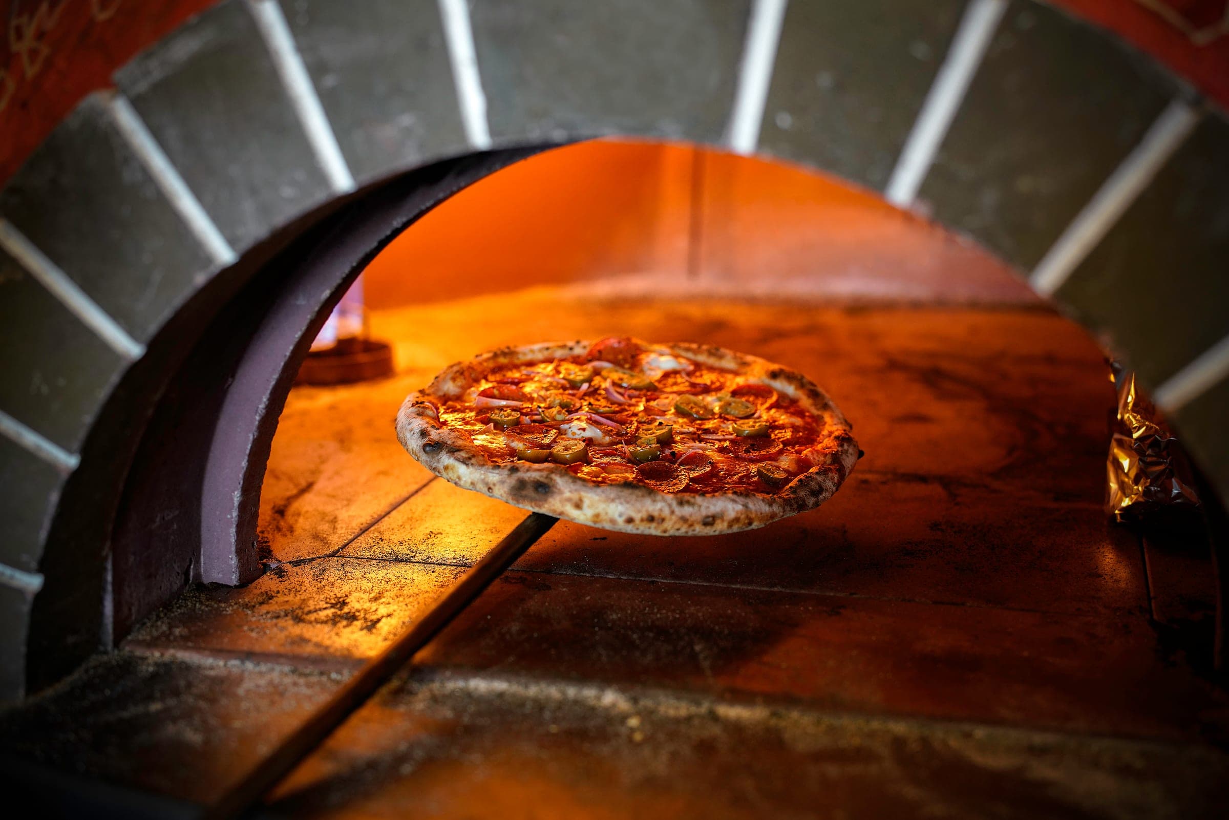 Pizza ur vedugnen — glöden lyser upp den nybakade degen